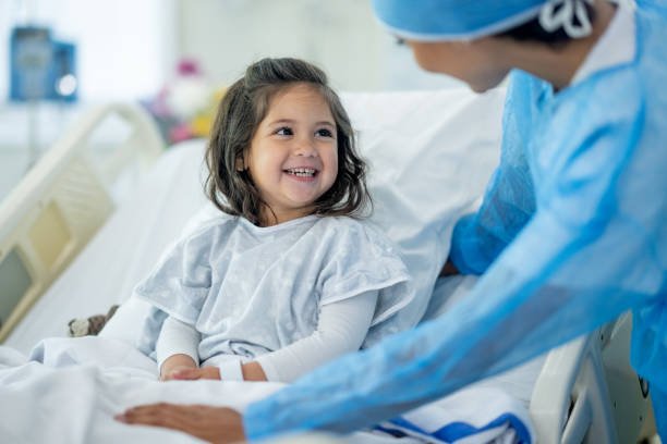 A female doctor of Indian decent checks in on a young female patient after her surgery.  The patient is sitting up in bed and appears happy.